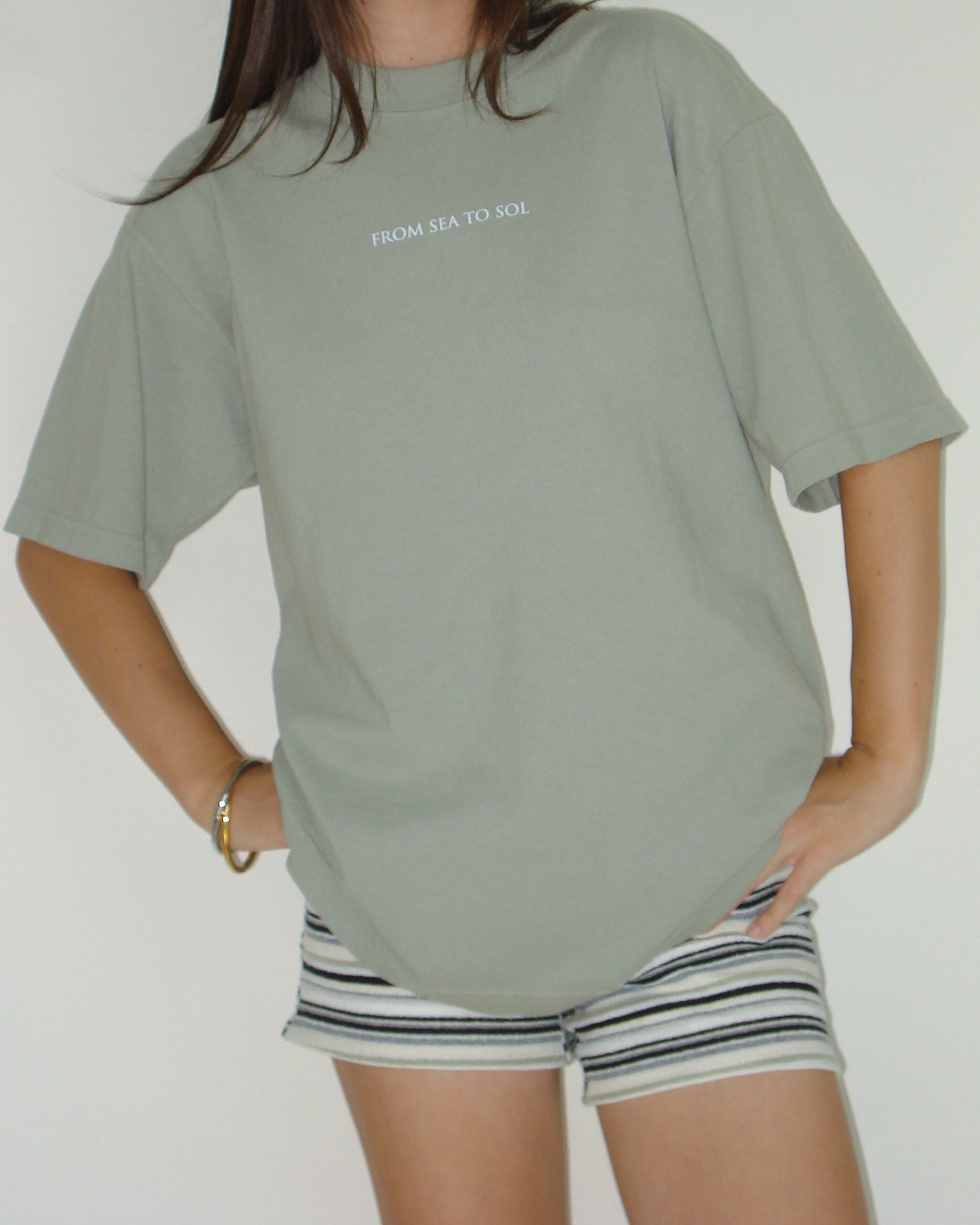 A person wearing a green t-shirt with the text 'FROM SEA TO SOL' on it, paired with striped shorts.