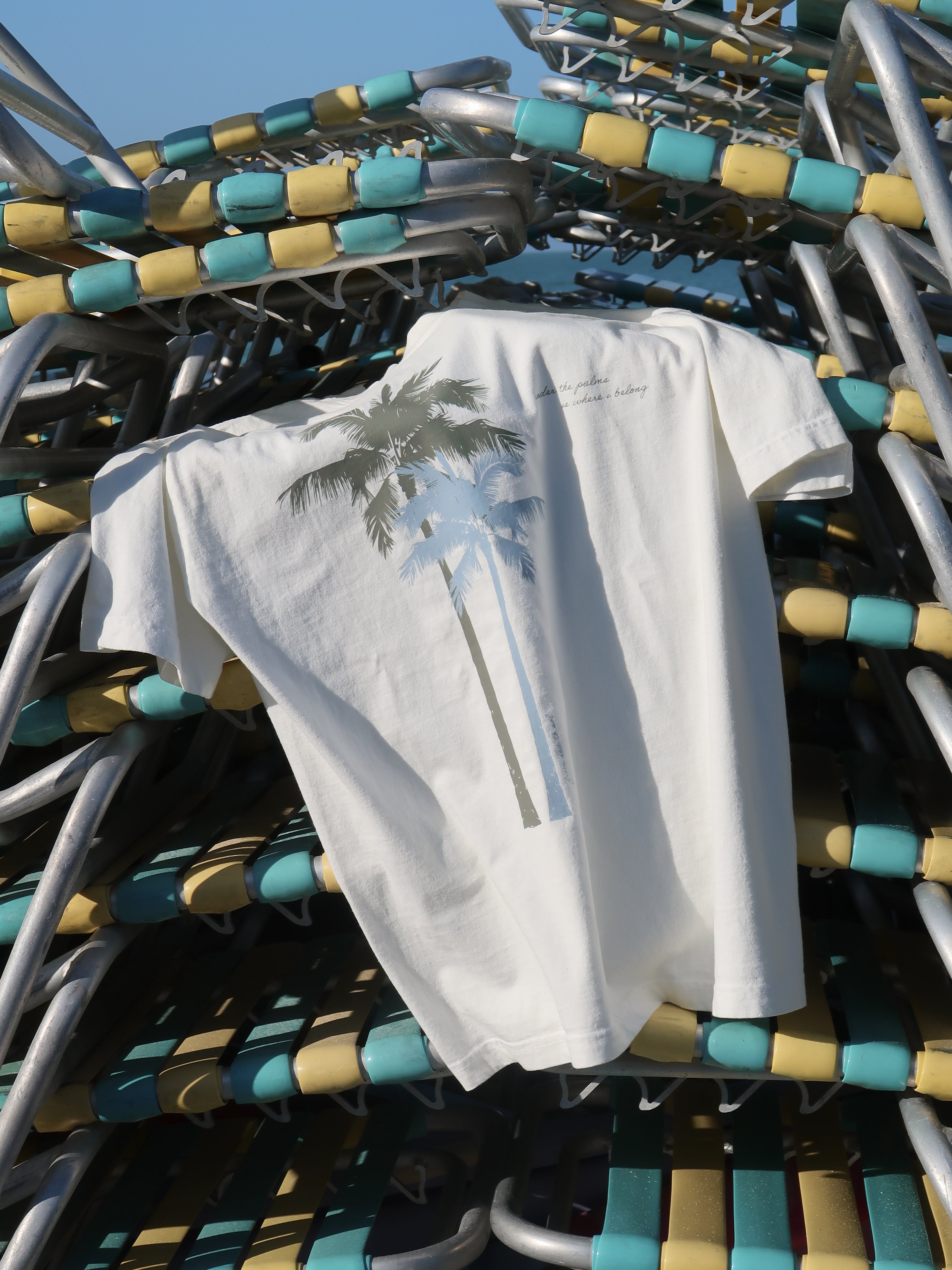 A woman wearing a white shirt with palm trees printed on it in green and blue paired with a striped short against a white background.