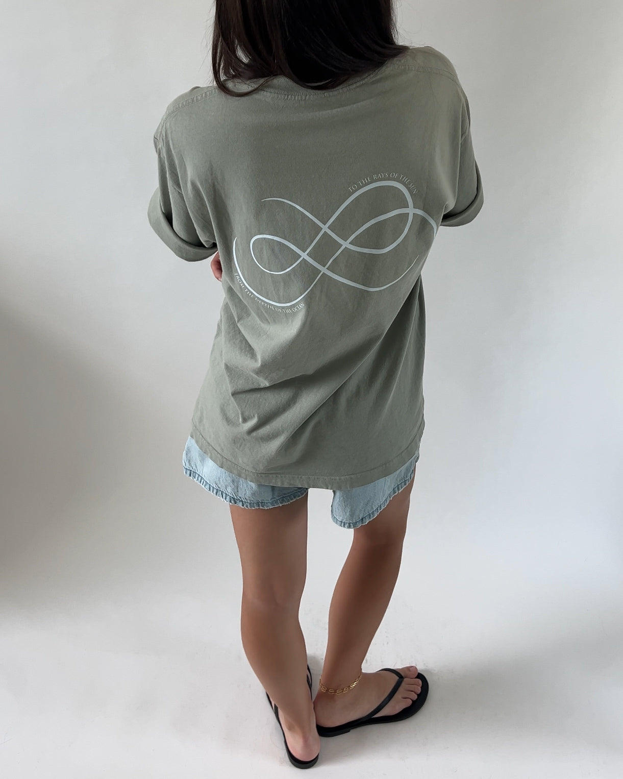 A person wearing a green t-shirt with the 'FROM SEA TO SOL' logo on the back and blue denim shorts, standing against a white background.