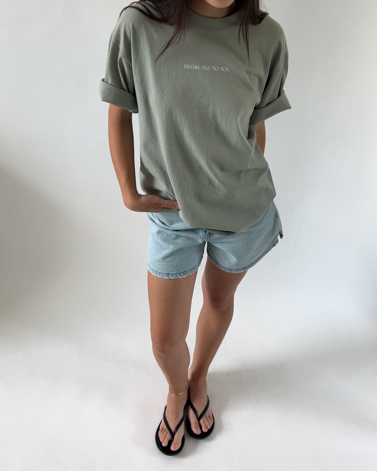 A person wearing a green t-shirt with the text 'FROM SEA TO SOL' on the front and blue denim shorts, standing against a white background.