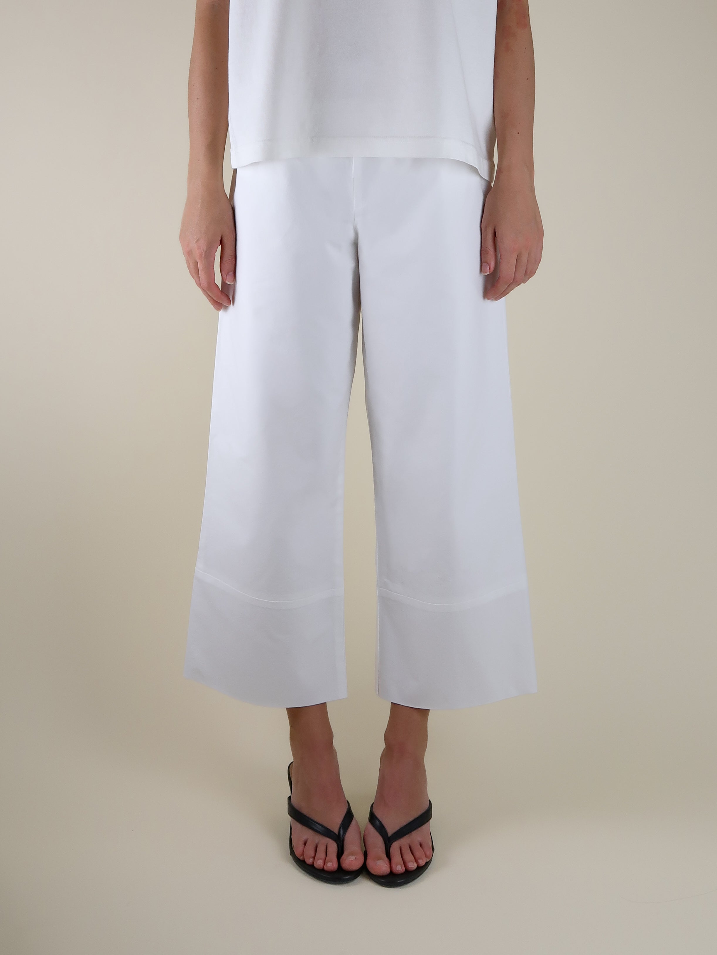 Person wearing white wide-leg pants on a beige background with black sandals