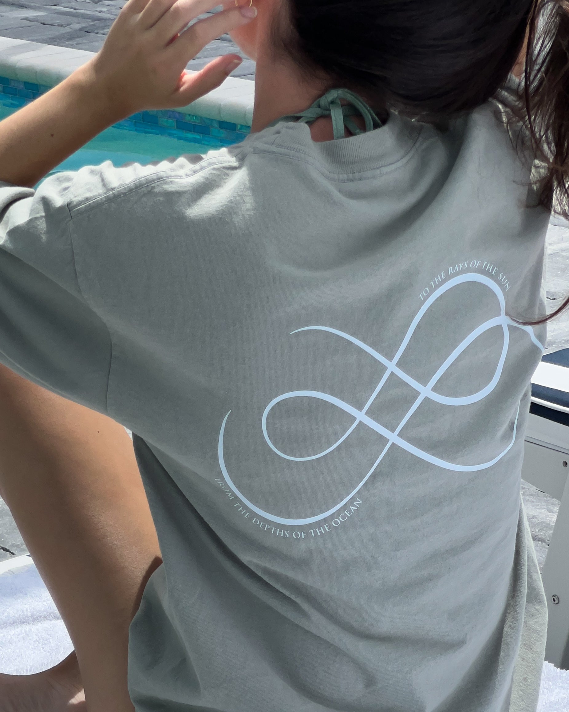 A person sitting near a pool wearing a green t-shirt with the 'FROM SEA TO SOL' logo on the back.