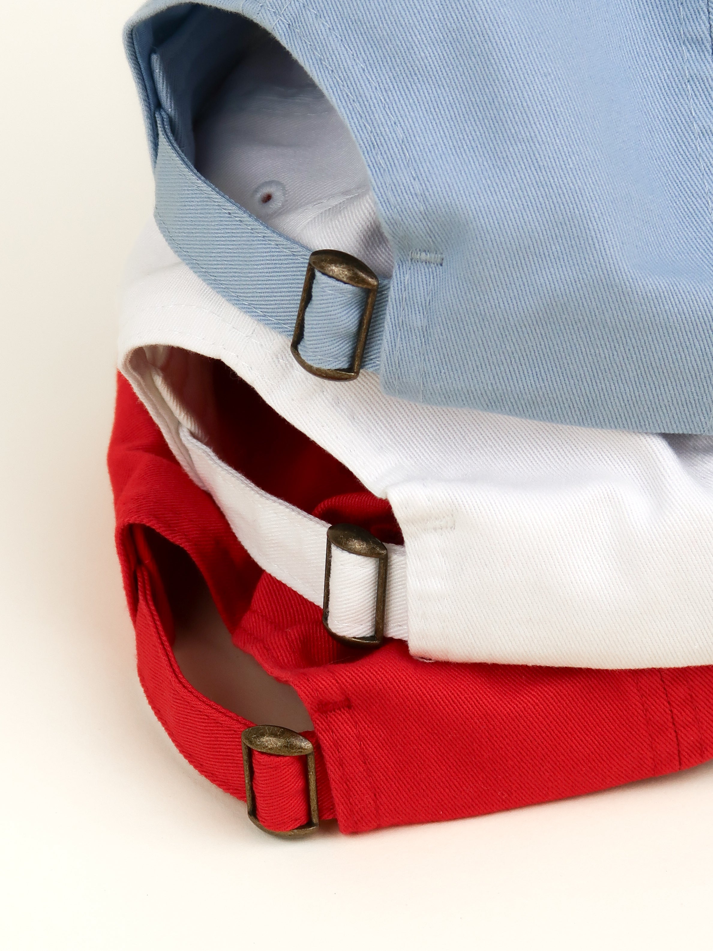 Close-up of a red, white, and blue cap with brass buckles on a light background