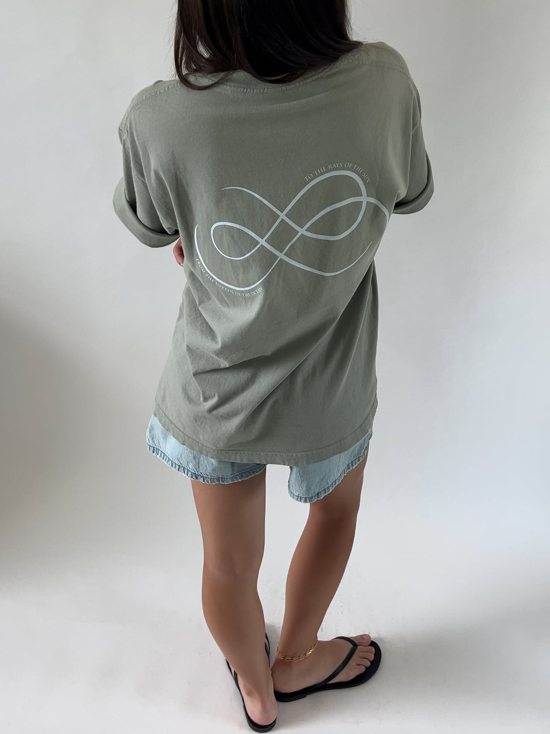 A person wearing a green t-shirt with the 'FROM SEA TO SOL' logo on the back and blue denim shorts, standing against a white background.